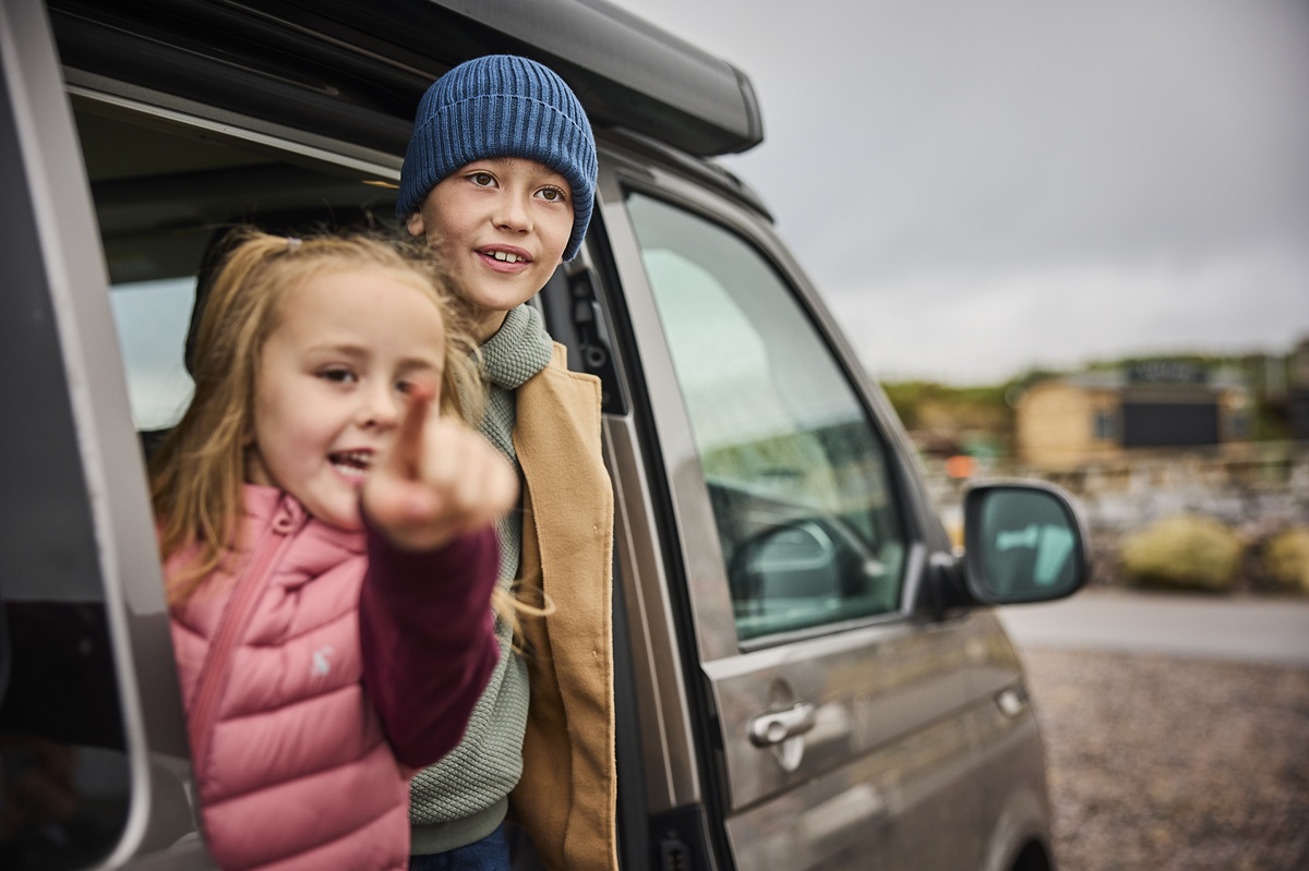 Children pointing at something at the horizon from a van.