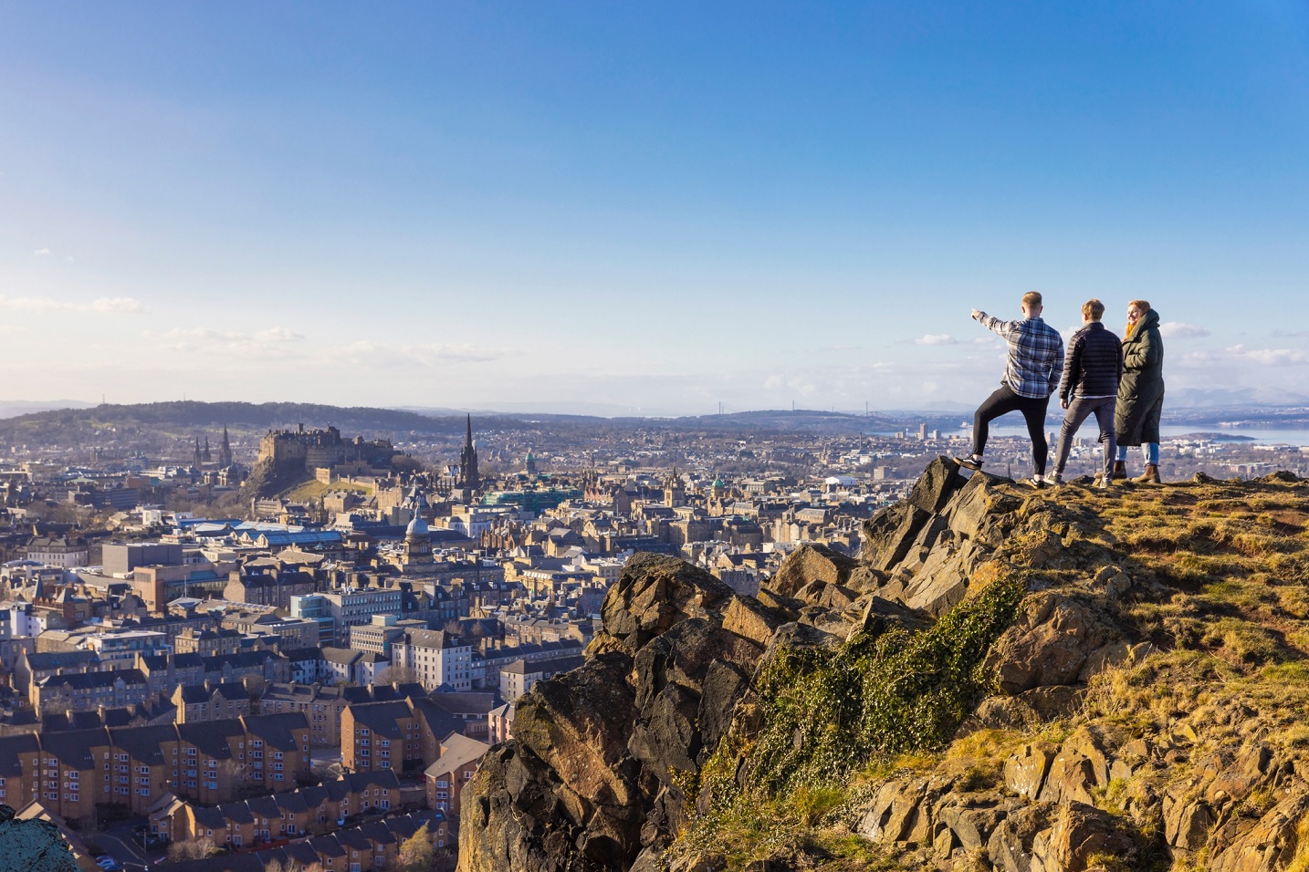 People standing at he top of a hill looking down towards a cityscape during the day