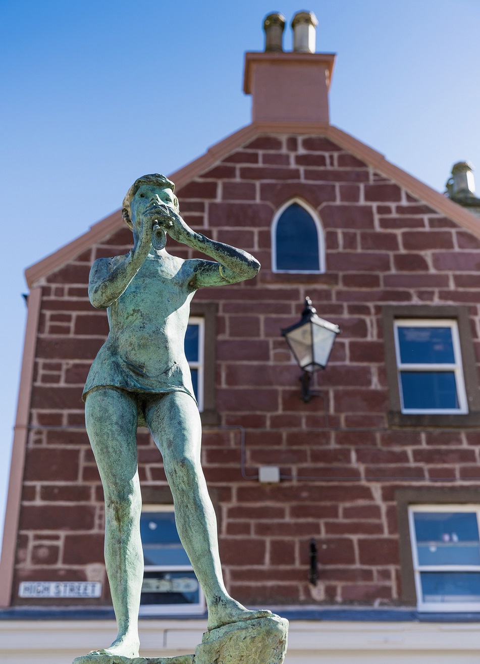 A statue of a young boy playing a musical instrument in a town centre