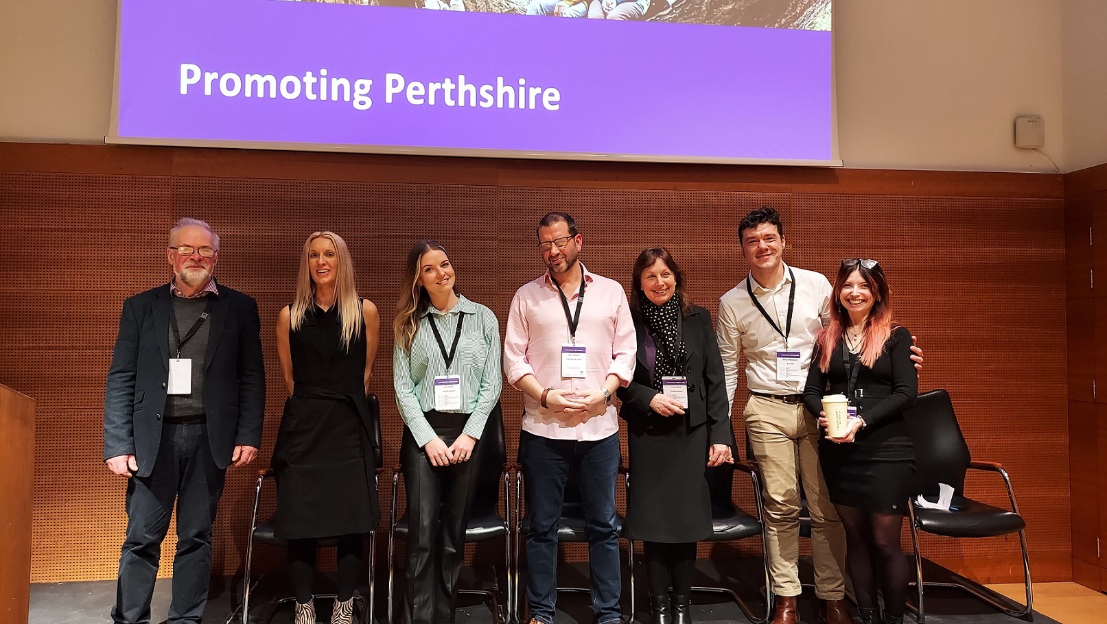 seven people standing in front of a large screen which reads "promoting Perthshire"