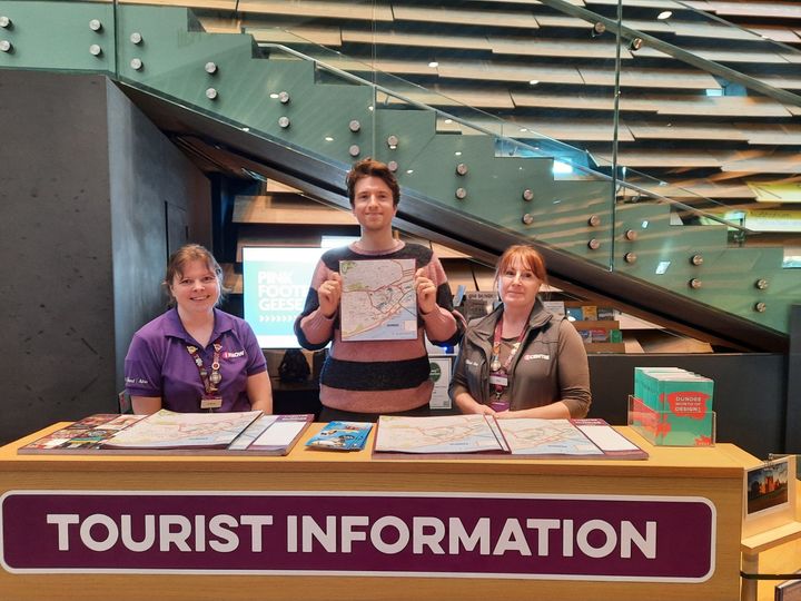 three people standing behind a welcome desk holding a map