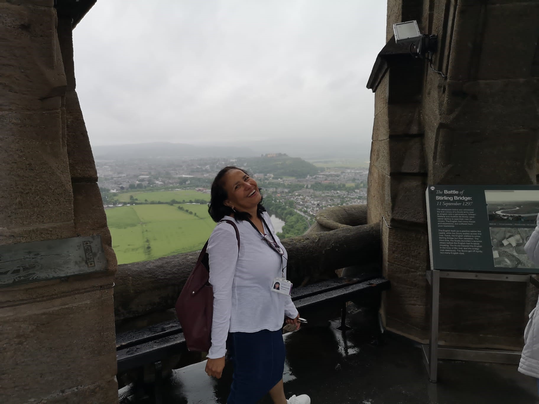 A member of the iCentre team standing at a viewing point at the top of the Wallace Monument with views of hills in the background