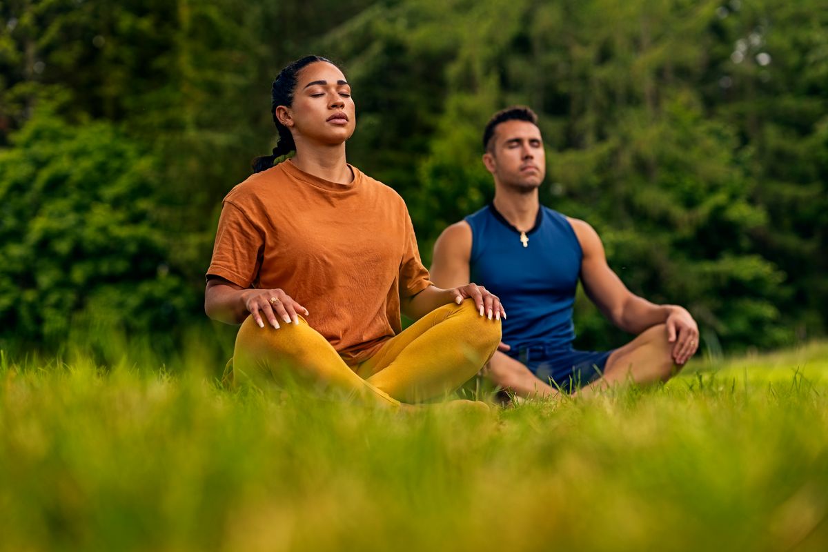 Two people doing yoga on a grassy field.