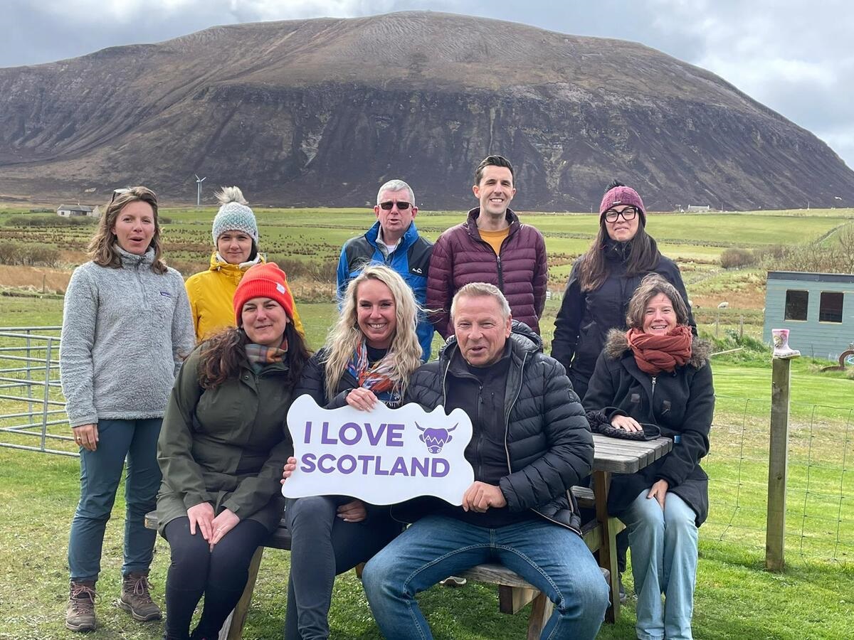 People pose with an I love Scotland sign in front of a hill on Orkney