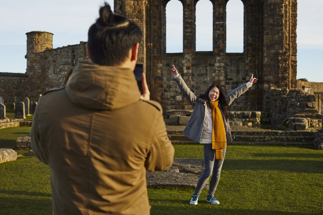 I person taking the pgoto of someone in the backround posing with hands in the air in front of a old building