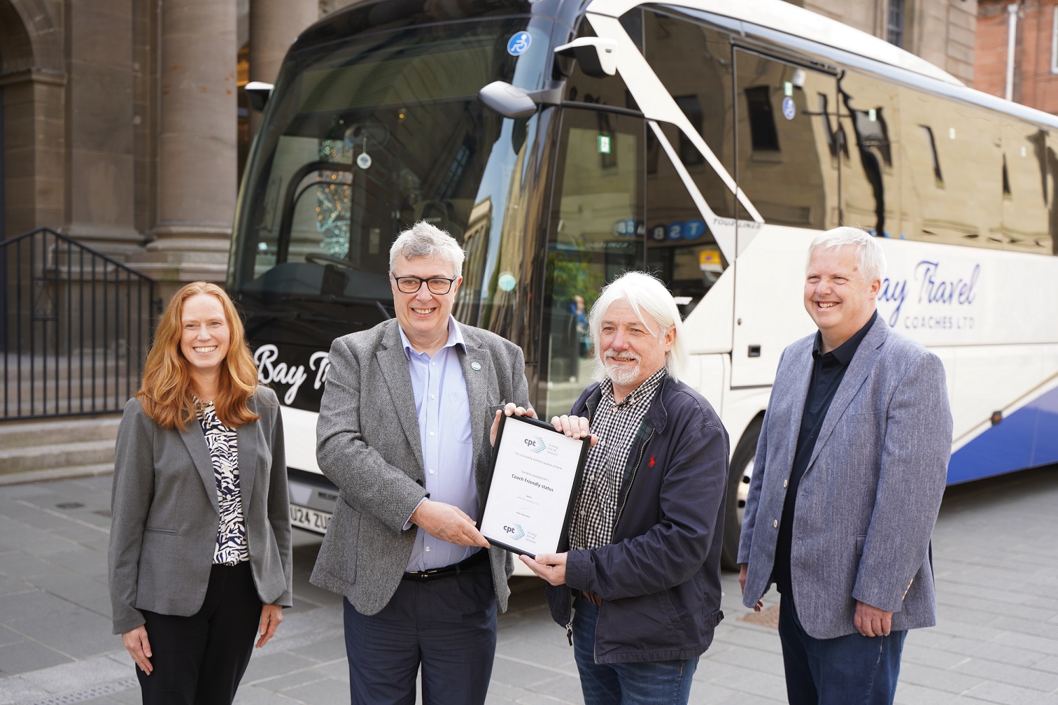 four people photographed in front of a coach outside