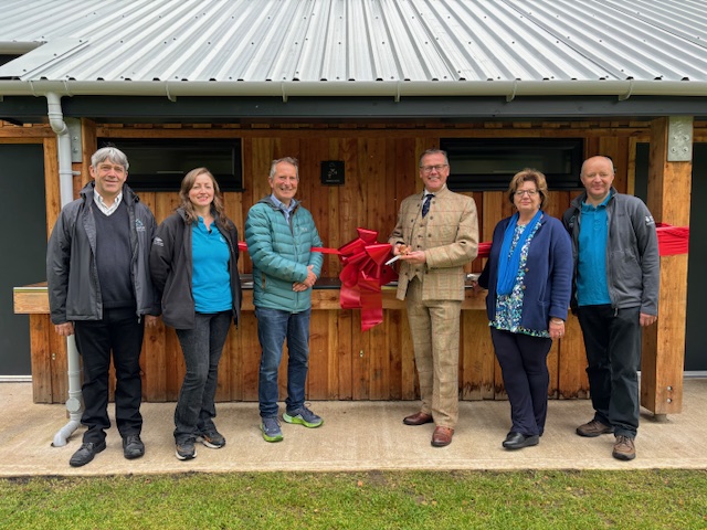 A group of people standing in front of a new building with a big red bow attached to the front of the building