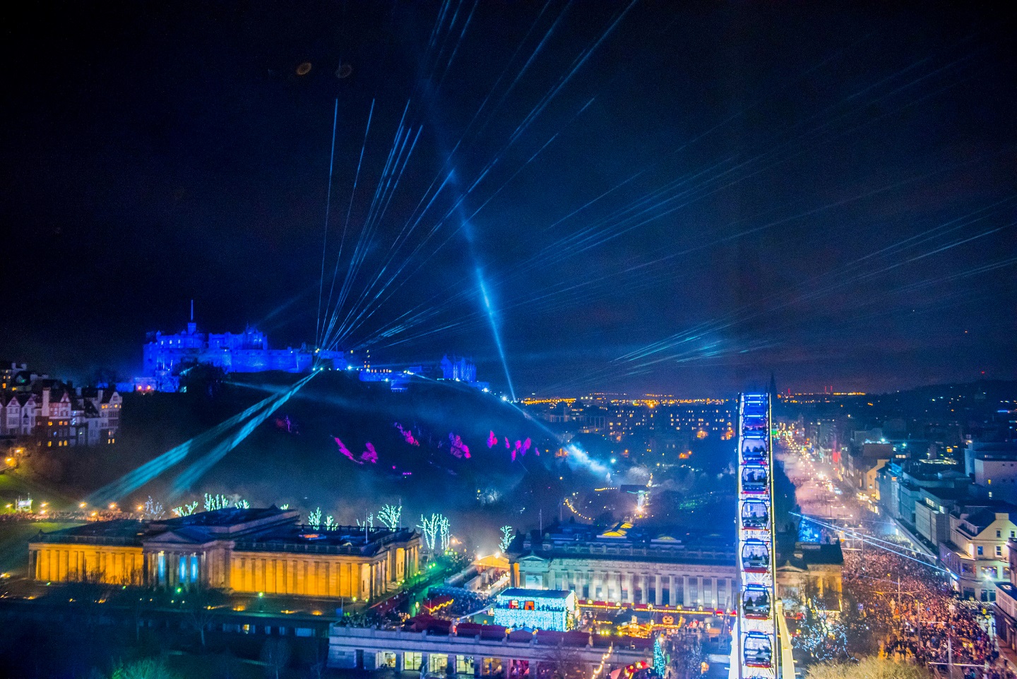 Overlooking Edinburgh Castle and Princes Street with revellers enjoying a light show from the Castle.