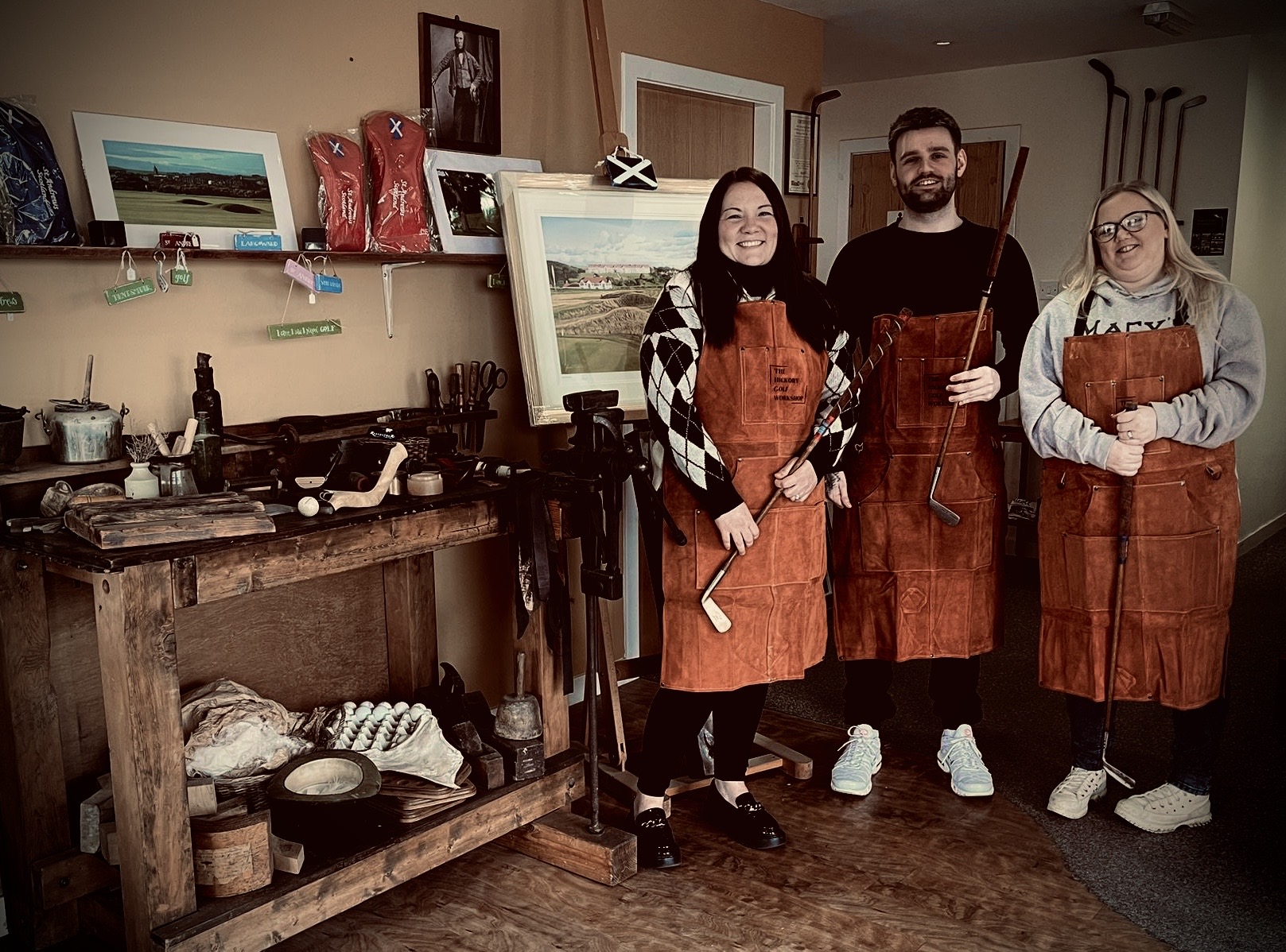 Three people standing in Hickory Workshop aprons with the Hickory golf clubs.