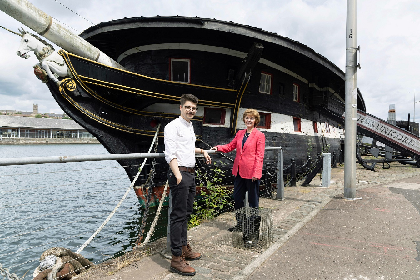Two people stnadin in front of a ship in a dock during the day